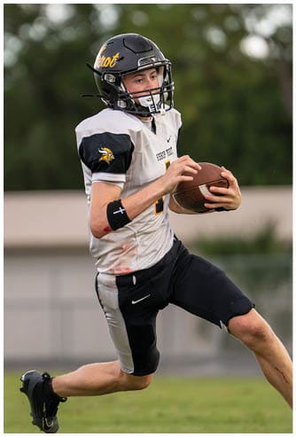 A person wearing a football uniform with the number 15 is running on a field while holding a football. Descripci n generada con IA