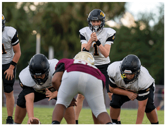 Three people wearing white football uniforms with black and yellow accents stand on the sidelines of a field, facing away from the camera. Descripci n generada con IA