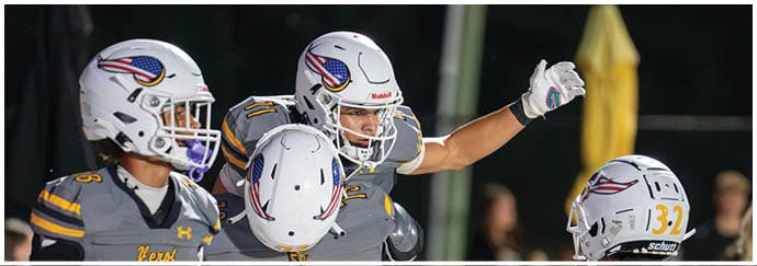 Adults in football uniforms are engaged in a game on a field with one player holding the ball and others preparing to block or tackle. Descripci n generada con IA