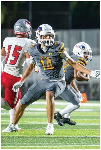 Several people wearing football uniforms are engaged in a close physical play on a grassy field under bright lights. Descripci n generada con IA