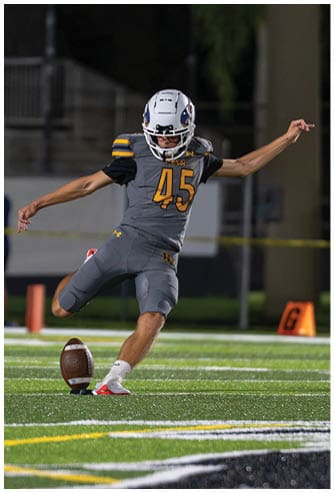 A person in a yellow football uniform is catching a football while other players in yellow and white uniforms watch on a field at night. Descripci n generada con IA