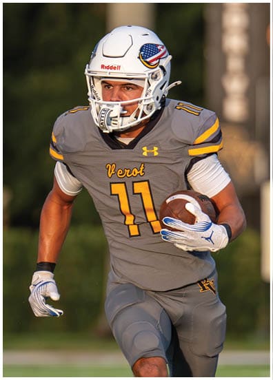 A person in a yellow football uniform with the number 11 is running with the ball while being pursued by another person in a white football uniform with the number 9 on a football field. Descripci n generada con IA