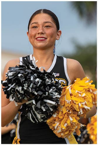 A person in a yellow and black football uniform is kicking a football on a field with other players and spectators in the background. Descripci n generada con IA