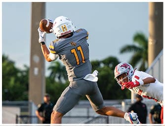Two people in yellow football uniforms are actively engaged in a play against two people in white football uniforms on a field with spectators in the background. Descripci n generada con IA