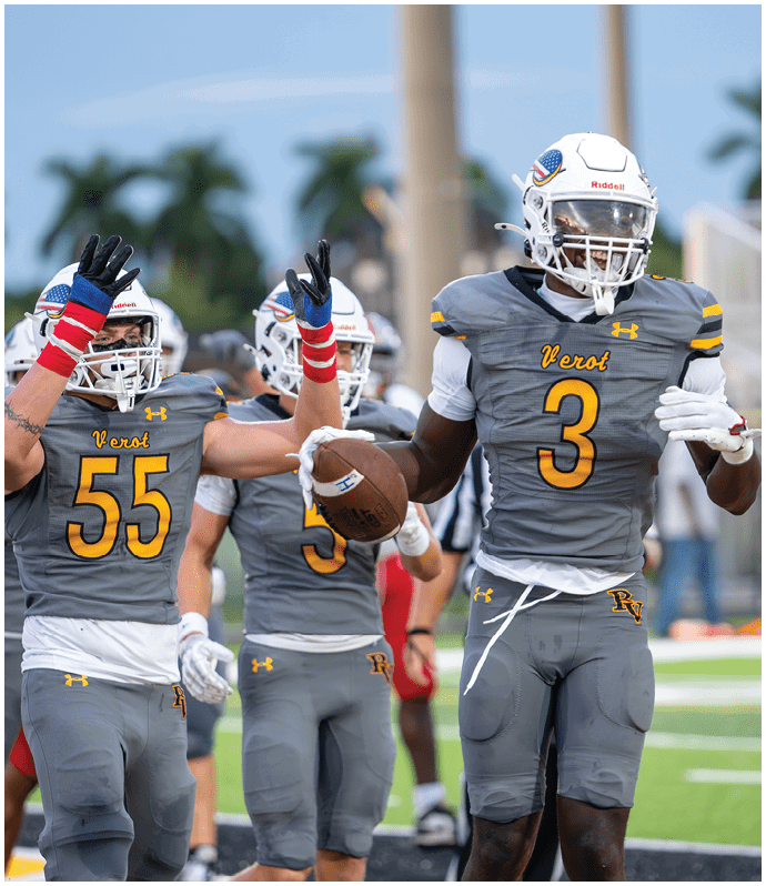 A person in a yellow football uniform with the number 28 is standing on a field near the end zone while a crowd of people in yellow and black clothing cheer behind a fence. Descripci n generada con IA