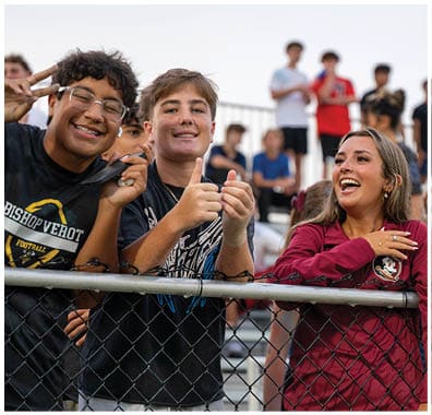 Two football players in yellow and black uniforms celebrate on the field while a crowd of people in similar colors cheer from the bleachers behind them. Descripci n generada con IA