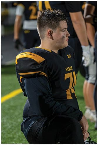 A person wearing a black and yellow football uniform with shoulder pads is kneeling on a field. Descripci n generada con IA