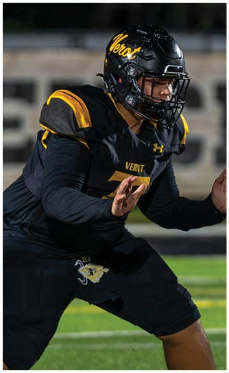 A person wearing a black and yellow football uniform is in a crouched position on a green field with white yard lines. Descripci n generada con IA