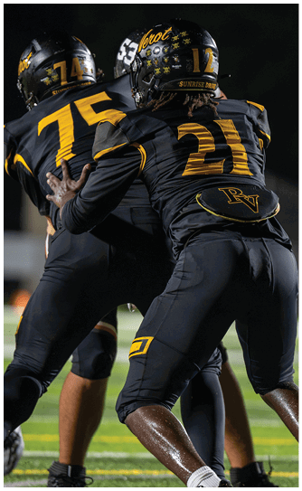 Two people wearing black and yellow football uniforms are engaged in a play on a well-lit field at night. Descripci n generada con IA