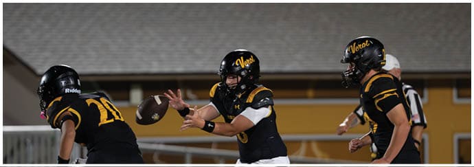 Three people in black and yellow football uniforms are on a field with one person passing a football to another. Descripci n generada con IA