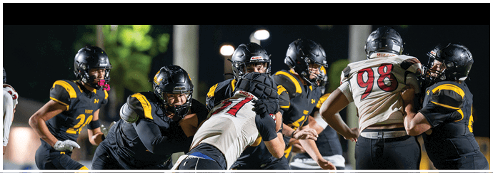 Several people wearing football helmets and uniforms are engaged in a play on a nighttime field. Descripci n generada con IA