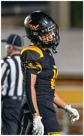 A person in a black and yellow football uniform and helmet stands on a field with a referee blurred in the background. Descripci n generada con IA