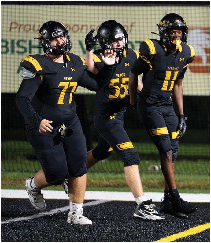 Three people in black and yellow football uniforms with helmets are on a field, appearing to be in motion during a game or practice. Descripci n generada con IA