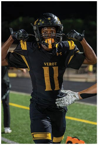 A person wearing a black football helmet with yellow skull decals and a yellow mouthguard is looking directly at the camera against a dark background. Descripci n generada con IA