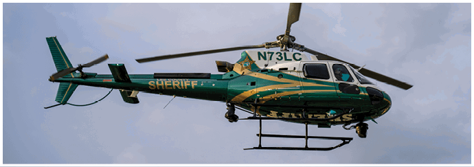 A green and white sheriff helicopter with the registration number N73LC is flying against a cloudy sky. Descripci n generada con IA