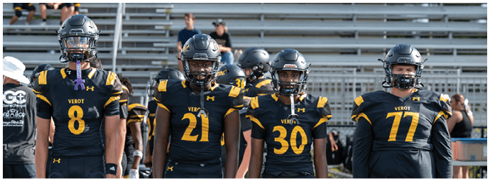 Four people wearing black and yellow football uniforms stand side by side on a field with empty bleachers in the background. Descripci n generada con IA