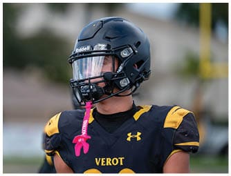 A person wearing a black football helmet with a clear visor and a black and yellow sports jersey is looking to the side. Descripci n generada con IA