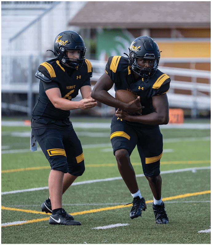 Two people in black and yellow football uniforms are on a field with one handing off a football to the other. Descripci n generada con IA