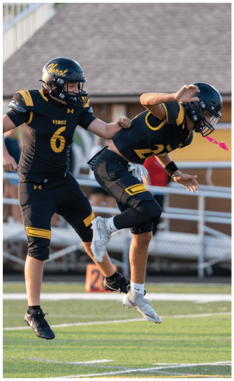Two people in black and yellow football uniforms are jumping on a field, appearing to celebrate or perform a coordinated action. Descripci n generada con IA
