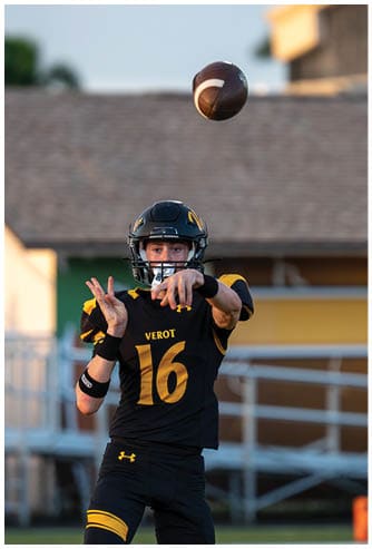 An adult wearing a black and yellow football uniform with the number 16 is throwing a football during a game or practice. Descripci n generada con IA