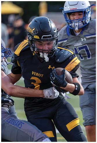 Two people in football uniforms are engaged in a play with one person holding the ball tightly while the other is closely pursuing. Descripci n generada con IA