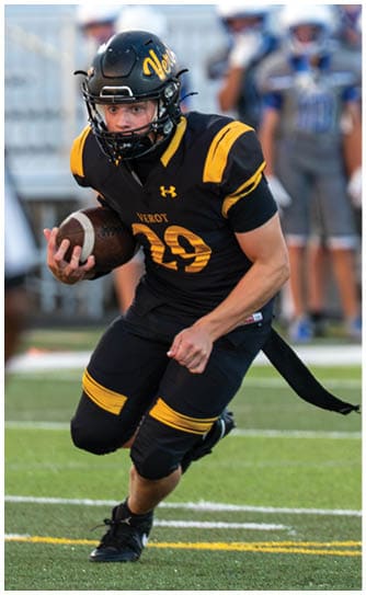 A person wearing a black and yellow football uniform is running on a field while holding a football. Descripci n generada con IA
