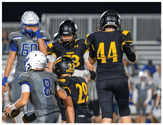 Several people in football uniforms are on a field with one person in a gray uniform holding a football while others in black and yellow uniforms surround them. Descripci n generada con IA