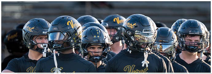 A group of people wearing black football helmets and matching black shirts with yellow “Verot Football" text stand closely together outdoors. Descripci n generada con IA