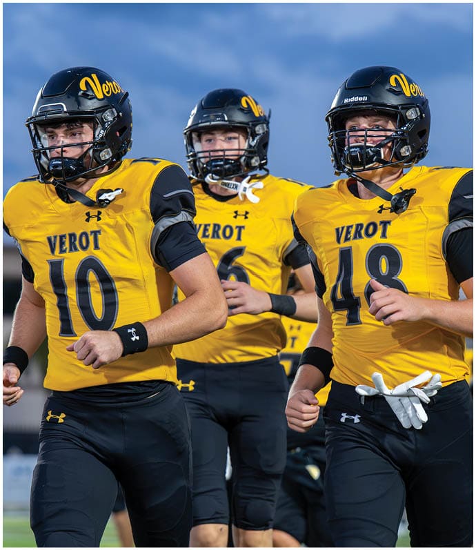 Three people wearing yellow and black football uniforms with helmets are running on a field. Descripci n generada con IA
