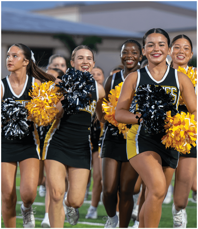 A group of people wearing yellow football uniforms stand together on a field at night, some holding helmets and others raising their hands. Descripci n generada con IA