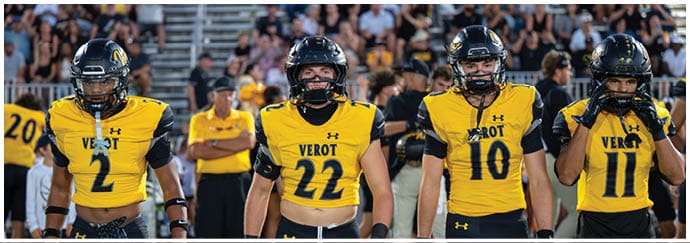 Three adults wearing yellow and black football uniforms and helmets stand on a field with a crowd in the background. Descripci n generada con IA