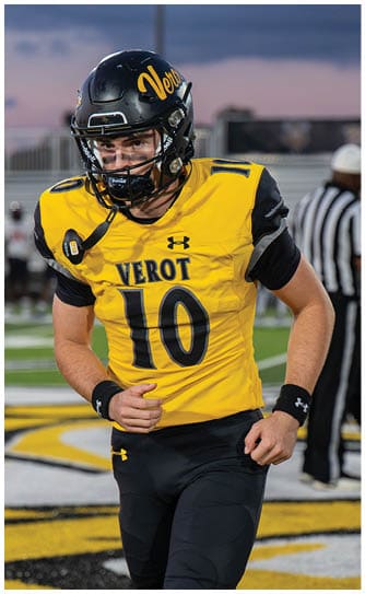 A person wearing a yellow and black football uniform with the word Verot and the number 10 on the jersey is standing outdoors with a black helmet and eye black under their eyes. Descripci n generada con IA