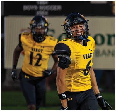 A person wearing a yellow and black football uniform with the number six is smiling and appears to be on a sports field. Descripci n generada con IA