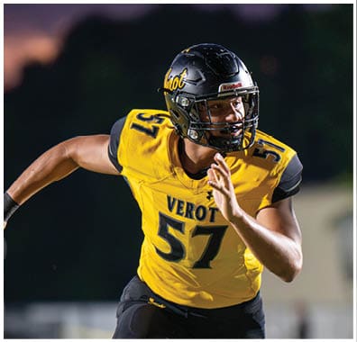 A person wearing a yellow and black football uniform with the number 57 is running on a field during a game at dusk. Descripci n generada con IA