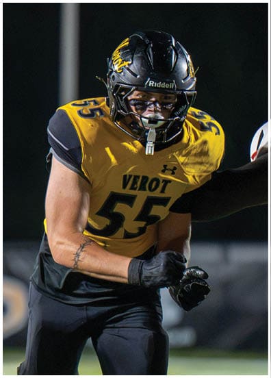 A person wearing a black football helmet and a yellow jersey with the number 55 and the word “VEROT" is focused and appears to be in action during a nighttime football game. Descripci n generada con IA