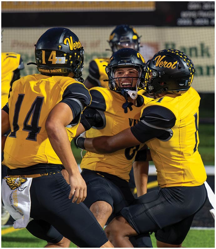 Three people in yellow and black football uniforms celebrate on a field with one person smiling broadly while being embraced by the others. Descripci n generada con IA