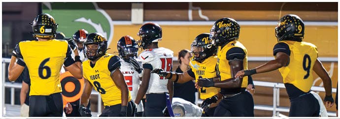 People wearing yellow and black football uniforms are gathered on a field during a game, with some players interacting with opponents in white and black uniforms. Descripci n generada con IA