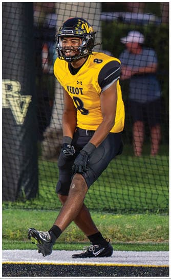 A person wearing a yellow and black football uniform with the number 8 is standing on a field near a goal post with the letters RV visible. Descripci n generada con IA