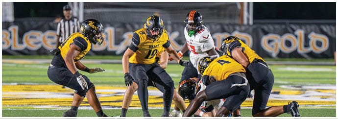 Several people in football uniforms are positioned on a field preparing for a play during a game. Descripci n generada con IA