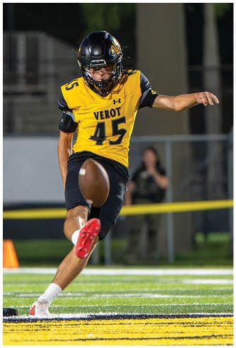 A person wearing a yellow sports jersey and black shorts is kicking a football on a field with yellow and black markings. Descripci n generada con IA