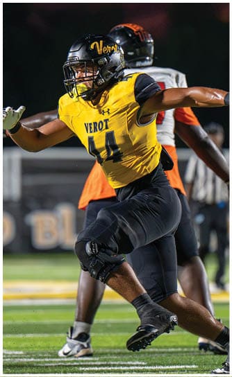 Two people in football uniforms are actively running on a field during a game, with one wearing a yellow and black jersey and the other in white and black. Descripci n generada con IA