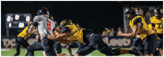 People in football uniforms are actively engaged in a play on a well-lit field during a nighttime game. Descripci n generada con IA
