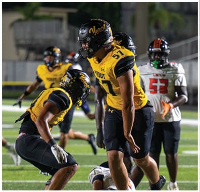 Several people wearing football uniforms and helmets are on a field, with two in yellow jerseys appearing to celebrate or communicate while another in a white jersey stands nearby. Descripci n generada con IA