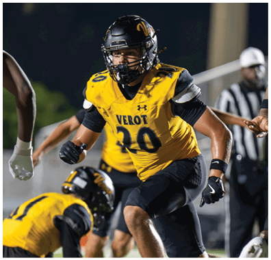 A person wearing a yellow and black football uniform with the number 20 is running on a field while another person in a similar uniform is crouched nearby. Descripci n generada con IA