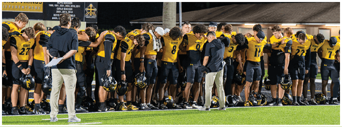 A group of people wearing yellow and black sports uniforms stand in a line on a green field with two individuals in casual clothing standing in front of them. Descripci n generada con IA