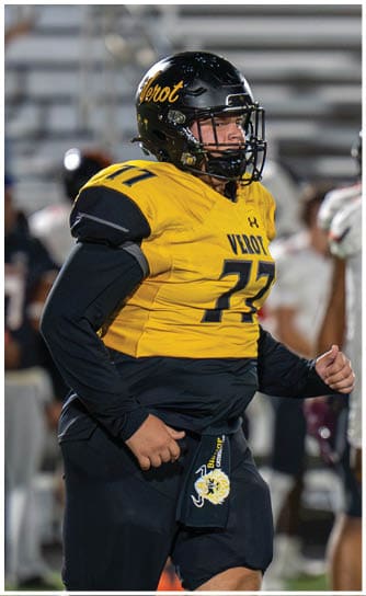 A person wearing a yellow and black football uniform with the number 77 is running on a field during a game. Descripci n generada con IA