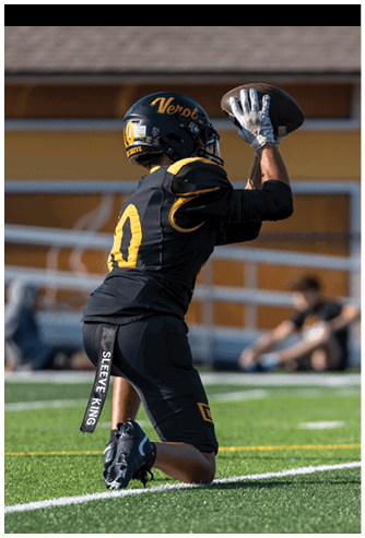 A person wearing a black and yellow football uniform with the number 10 is kneeling on a field while catching a football. Descripci n generada con IA