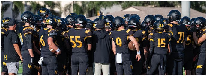 A group of people wearing black and yellow football uniforms stand closely together on a field, facing away from the camera. Descripci n generada con IA