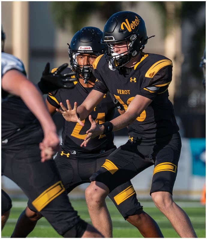 Several people in football uniforms are actively engaged in a play on a grassy field during a game. Descripci n generada con IA