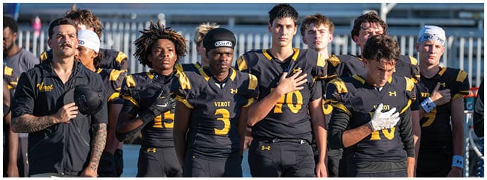 A group of people wearing black and yellow sports uniforms stand side by side with some holding their hands over their chests in an outdoor setting. Descripci n generada con IA